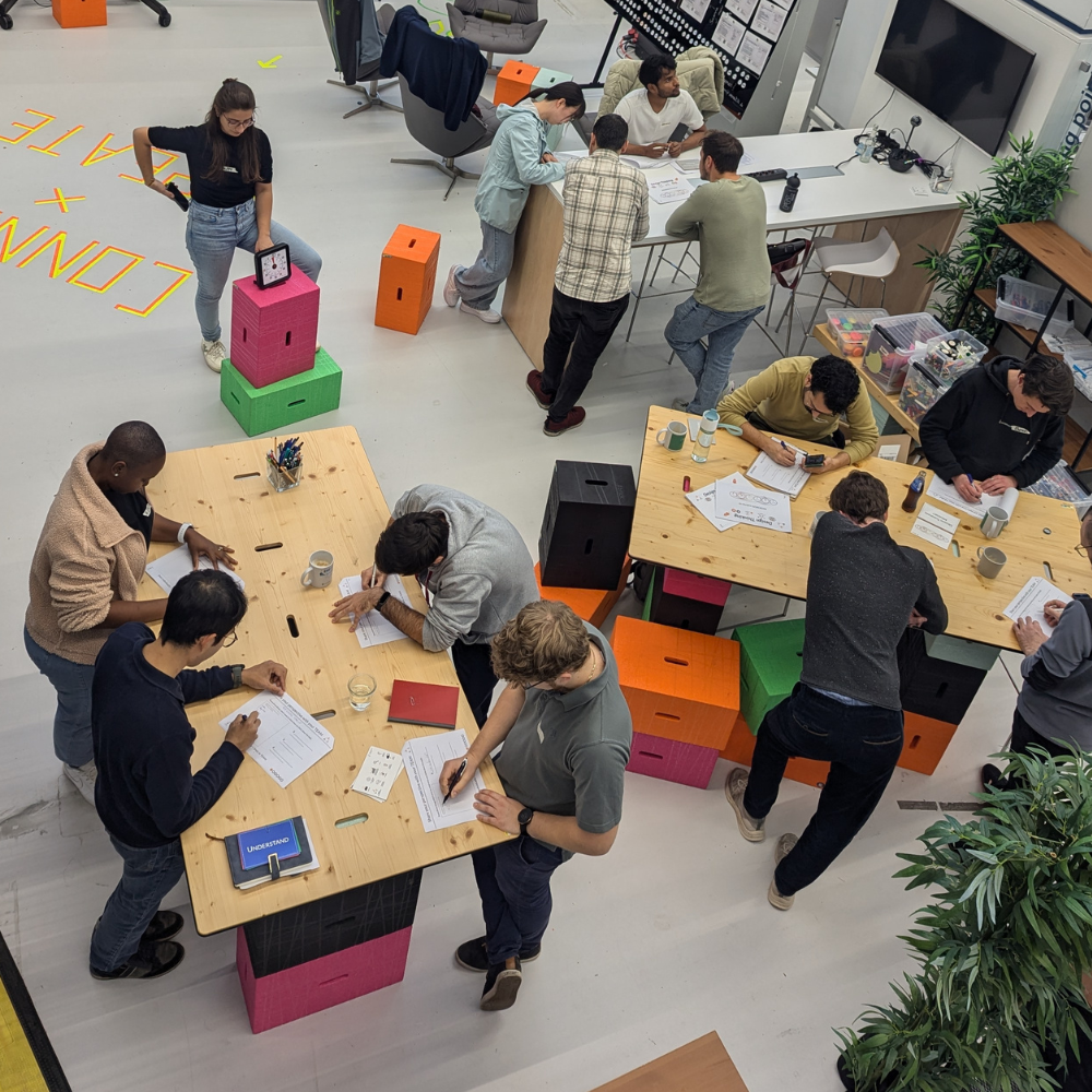 Ein Foto von mehreren Personen bei einem Workshop, die um Tische herum stehen und arbeiten.